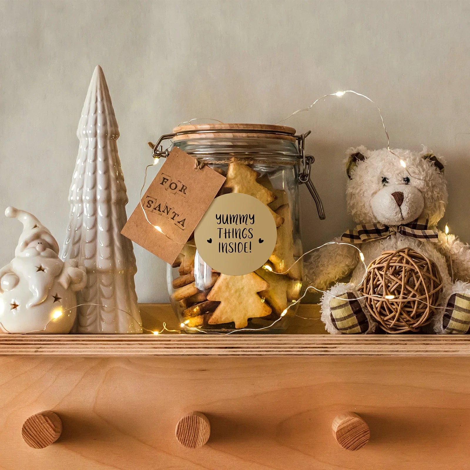 Christmas cookies in labeled jar with holiday decor, teddy bear, and string lights on shelf