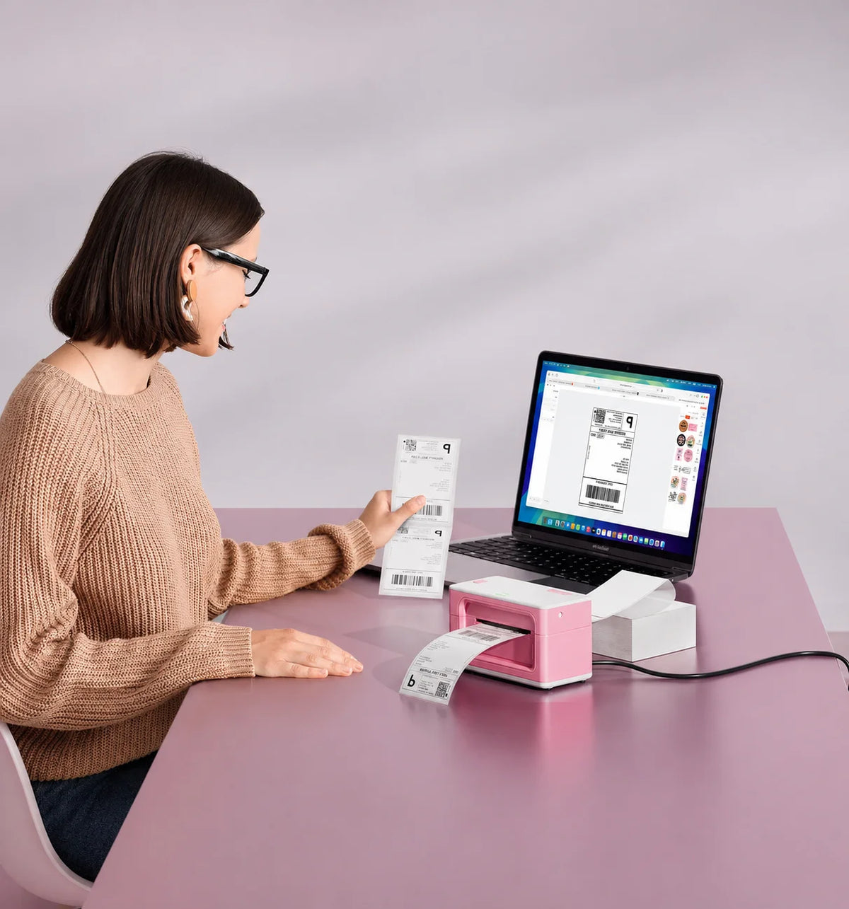 Woman using a laptop with a Munbyn pink label printer on a pink table.