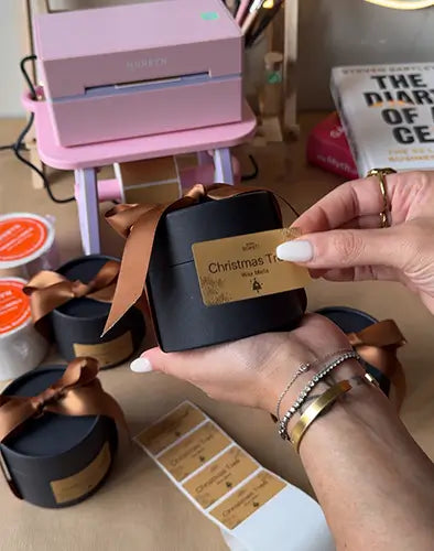 Person holding a black gift box with a Munbyn gold label, surrounded by festive decor.